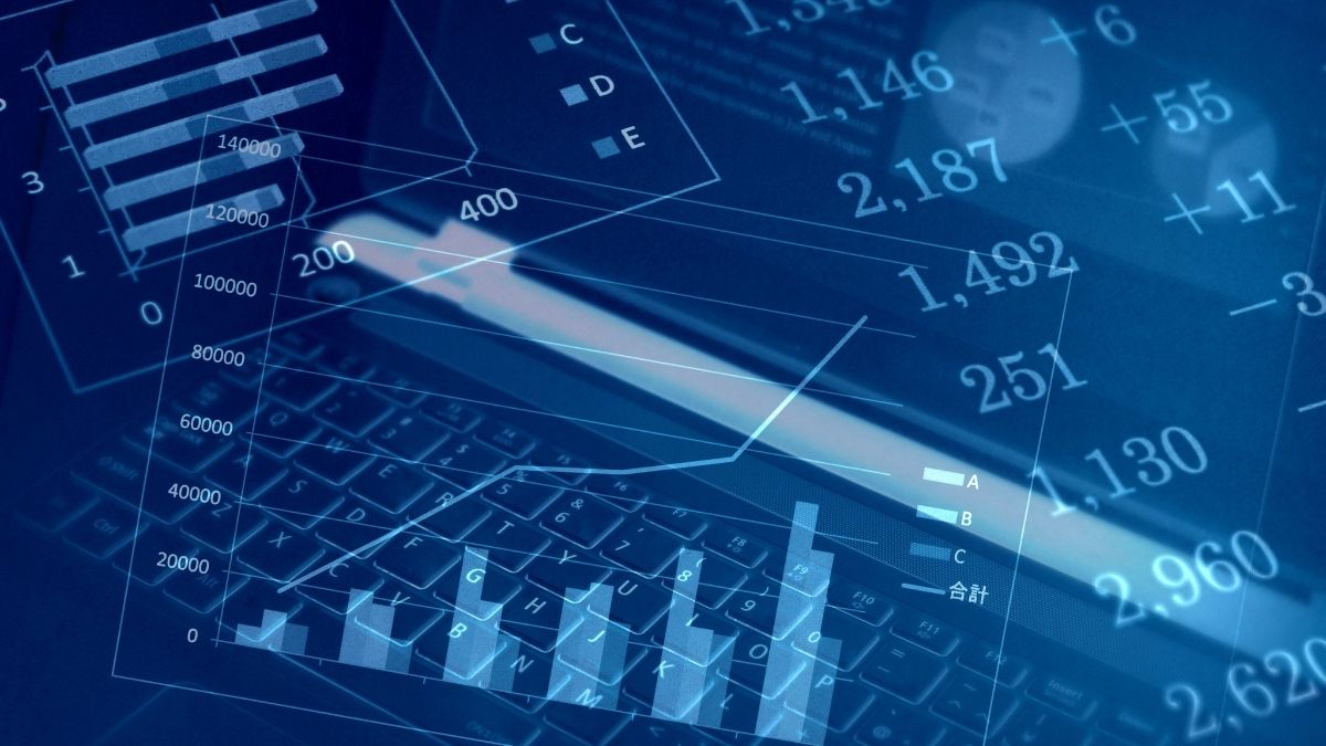 Grafici a barre e a linee con valori numerici sovrapposti alla tastiera di un computer portatile, in tonalità blu.