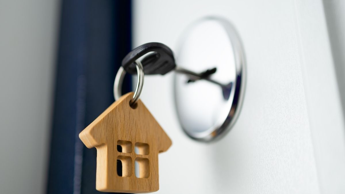 Chiave inserita nella serratura di una porta bianca con un portachiavi di legno a forma di casa.
