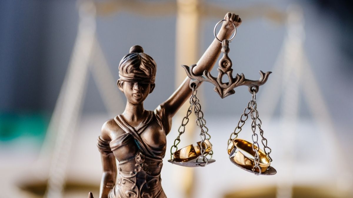 Statuetta della Giustizia bendata con anelli dorati sui due piatti della bilancia.
