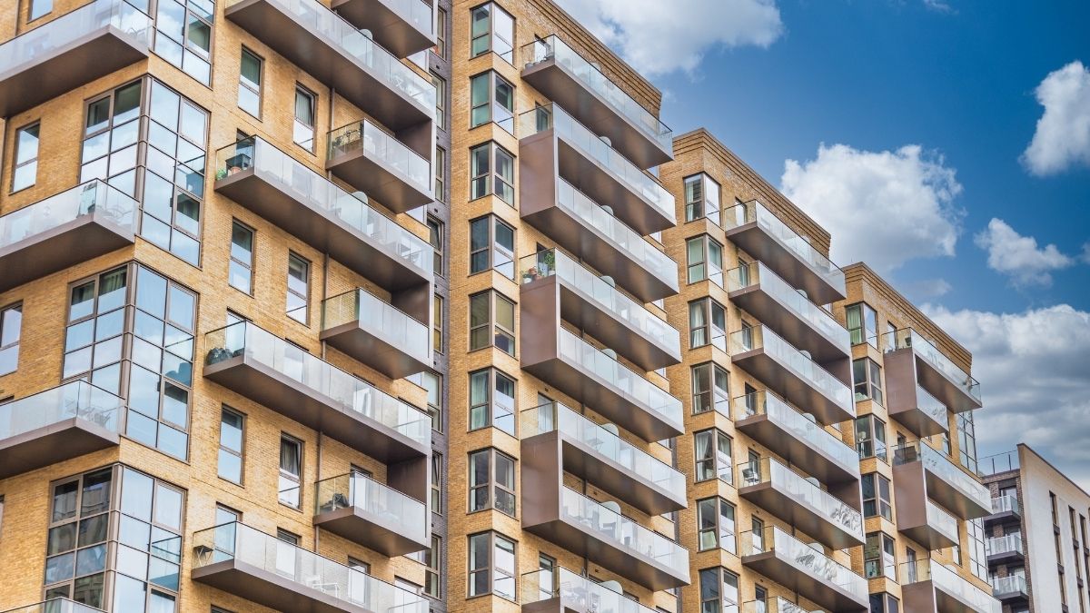 Edificio residenziale a più piani con facciate in mattoni chiari, grandi finestre e balconi con parapetti in vetro.
