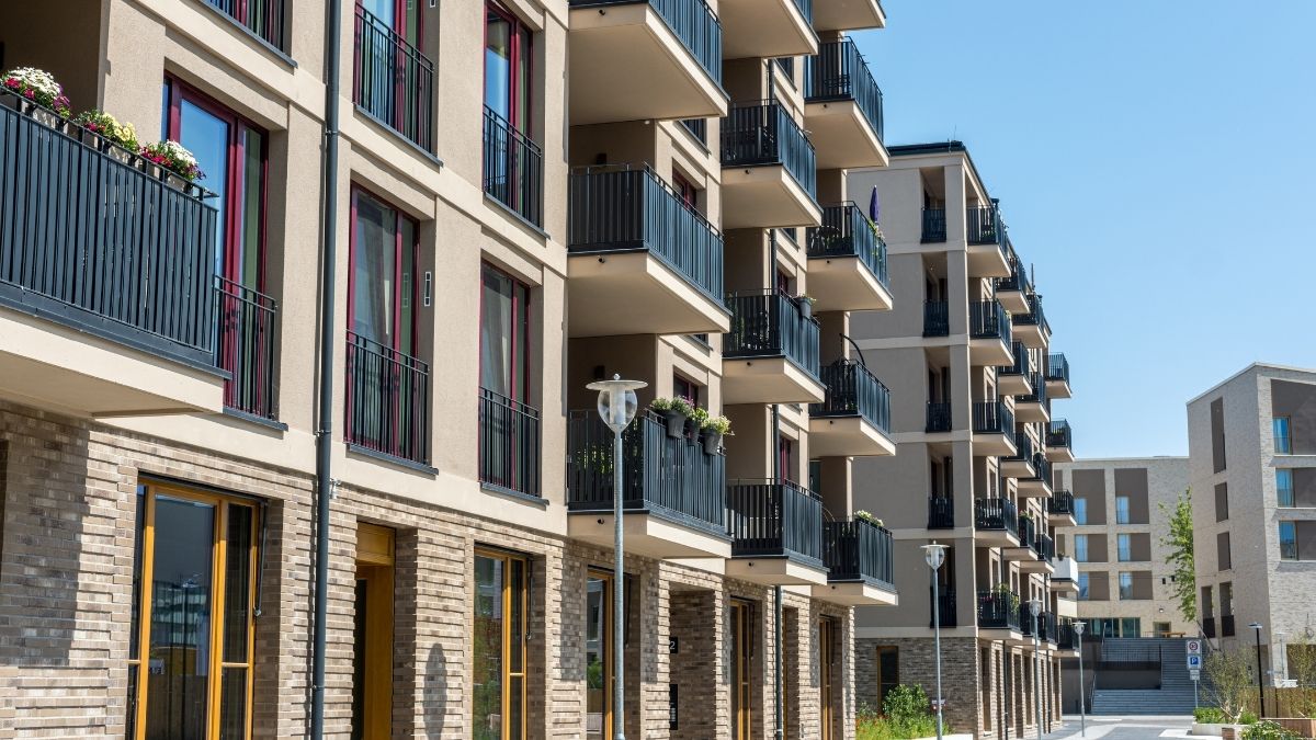 Palazzi residenziali con balconi e ringhiere scure affacciati su un percorso pedonale con lampioni e fioriere.