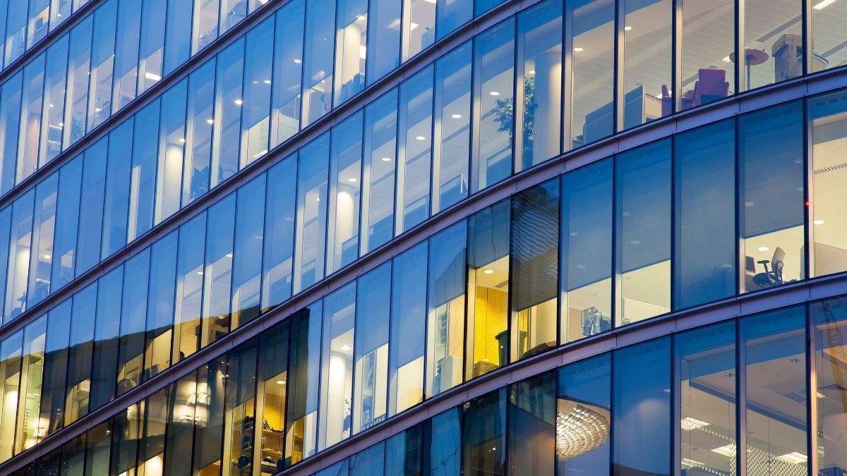 Facciata vetrata di un edificio per uffici con finestre azzurre e ambienti interni illuminati.