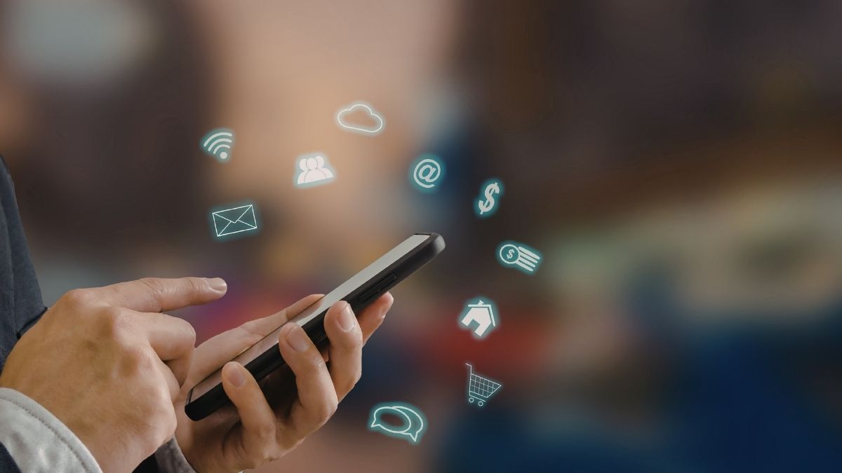 Mani che usano uno smartphone con icone luminose sovrapposte di messaggi, posta, acquisti, denaro e connessione.