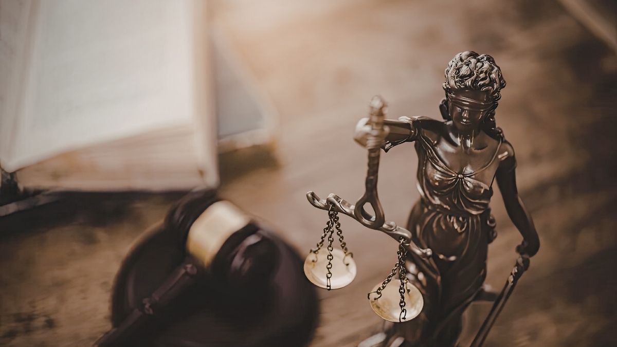 Statuetta della Giustizia bendata con bilancia e spada, accanto a un martelletto e a un libro aperto su un tavolo.